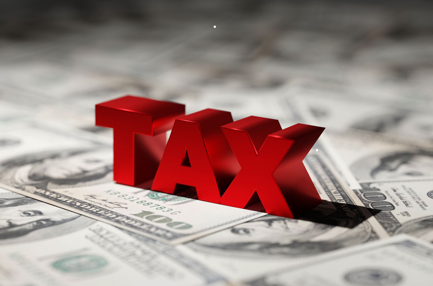 Red block letters spelling the word tax sitting atop U.S. dollar bills