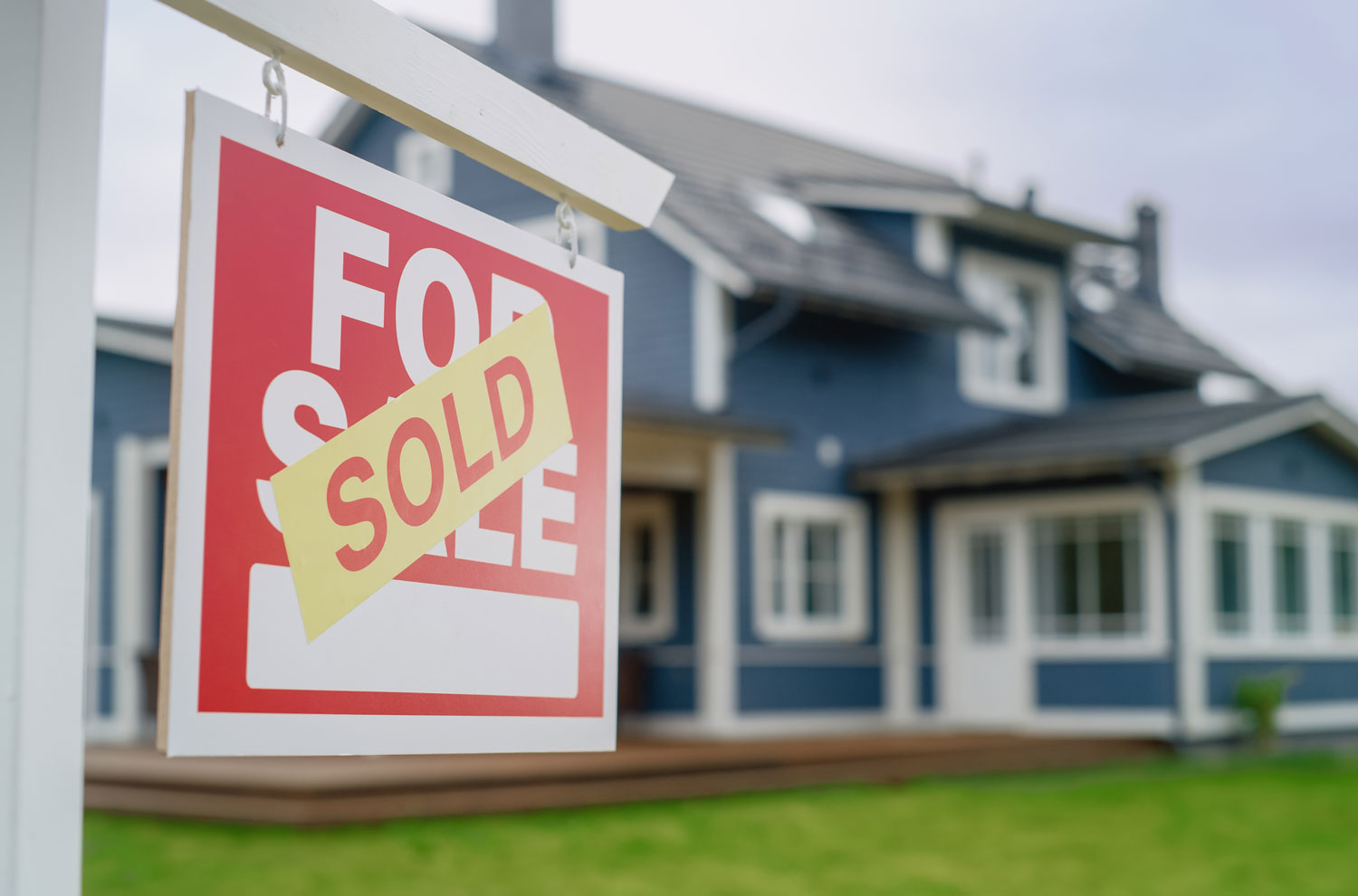 Closeup of sold yard sign with blue house in background