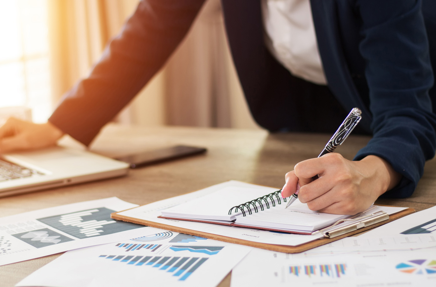 Businesswoman hand writing in notebook on desk with other paperwork